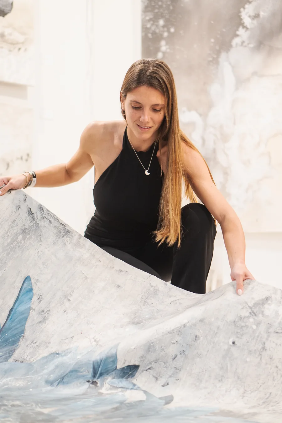 Belén Marcuzzi levantando un lienzo sin bastidor en su taller, con obras de la serie Terra en la pared detrás
